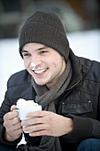 Junger Mann trinkt Kakao mit Schlagsahne