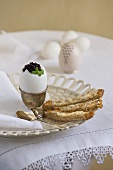 Osterfrühstück mit gekochtem Ei garniert mit Kaviar und Brotstreifen