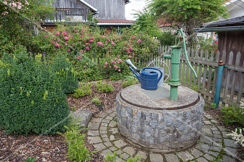 Laendlicher Garten mit Brunnen aus Naturstein gemauert, Schwengelpumpe