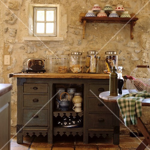 Alte Küchenkommode mit Vorratsgläsern vor rustikaler Natursteinwand