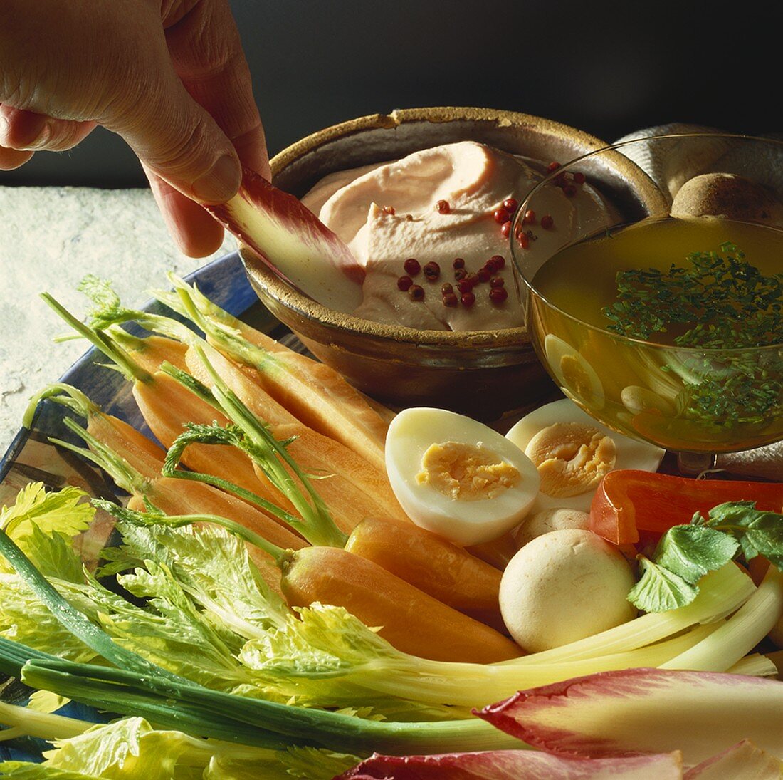 Hand holding radicchio leaf over dip on a vegetable platter