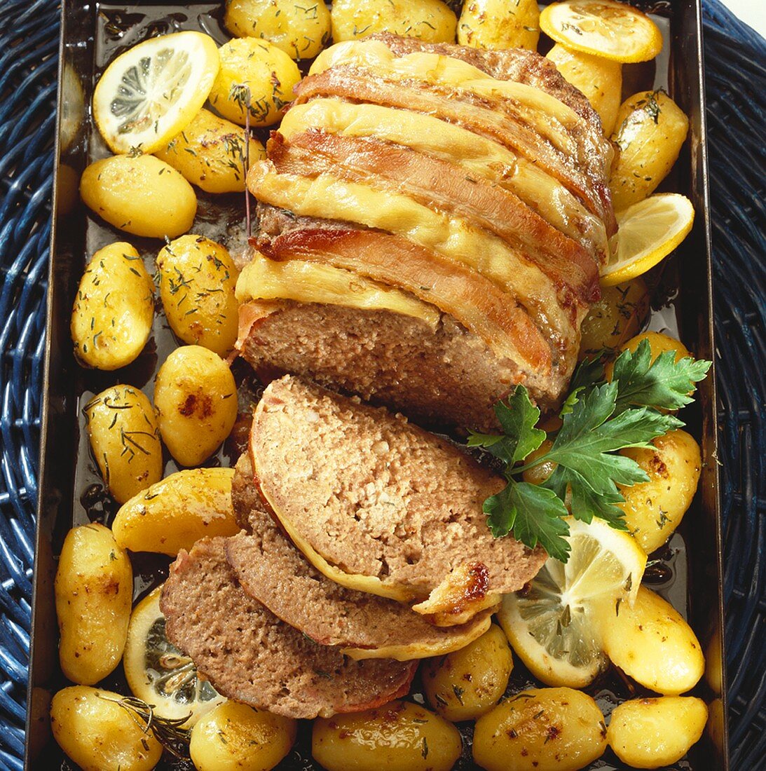 Bacon-wrapped meatloaf with potatoes on a baking tray