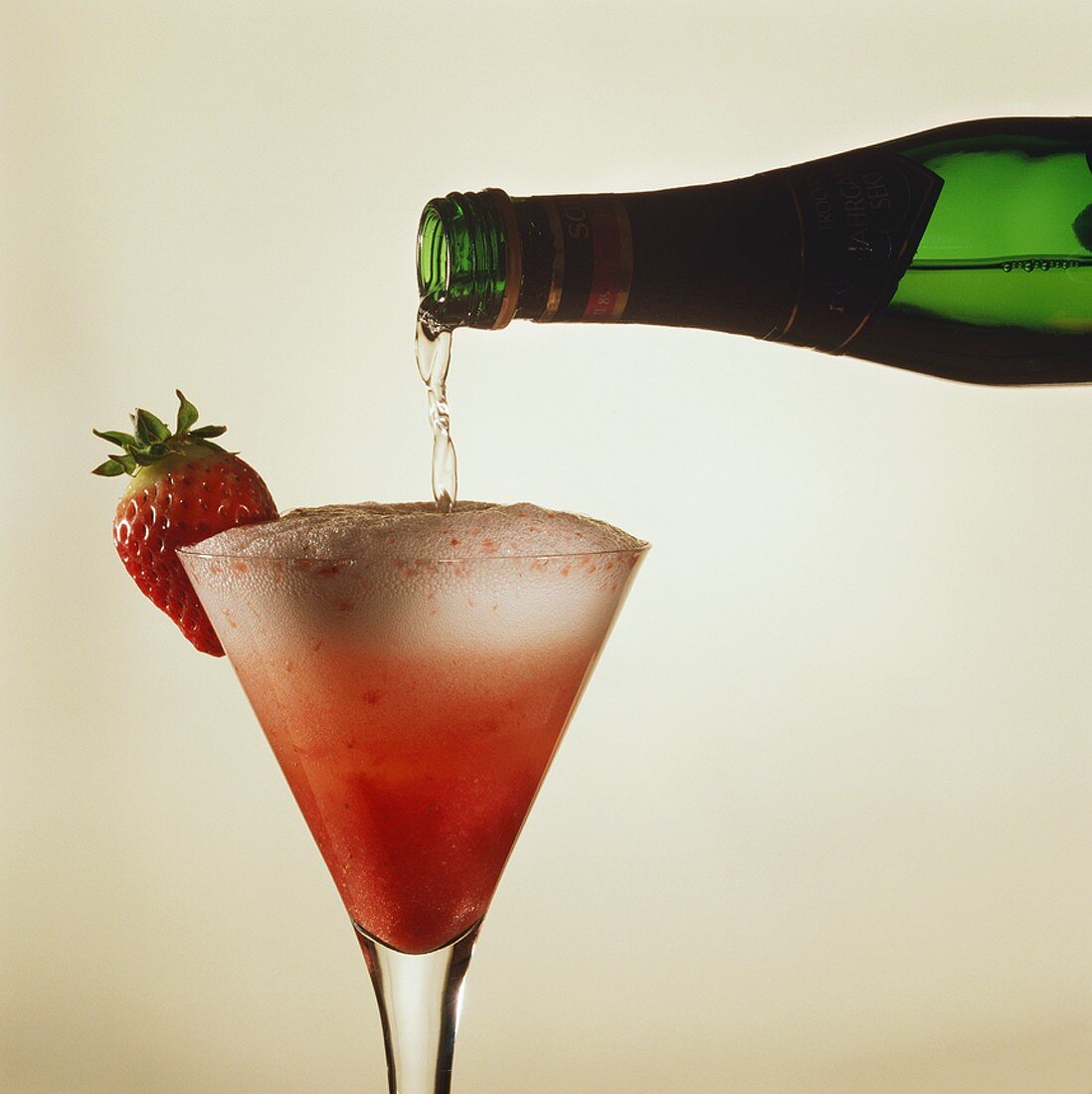 Sparkling wine being poured onto strawberry puree in wine glass