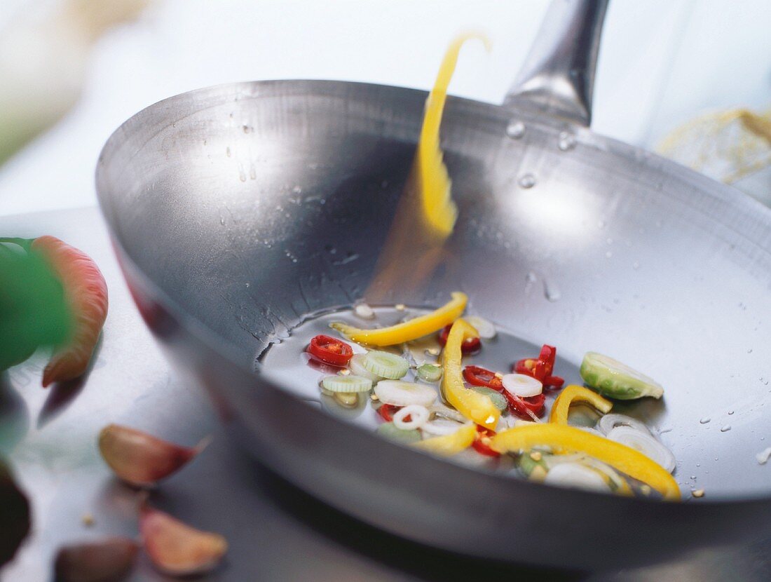 Slice of pepper falling into wok with vegetables & sesame oil