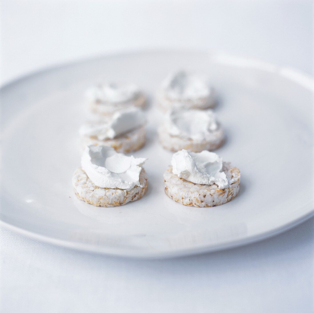 6 rice cakes spread with soft cheese on white plate