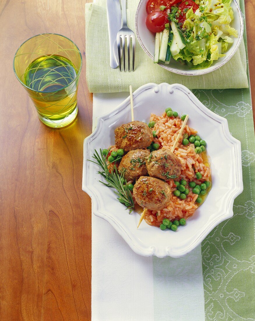 Skewered meatballs on tomato rice with peas and rosemary