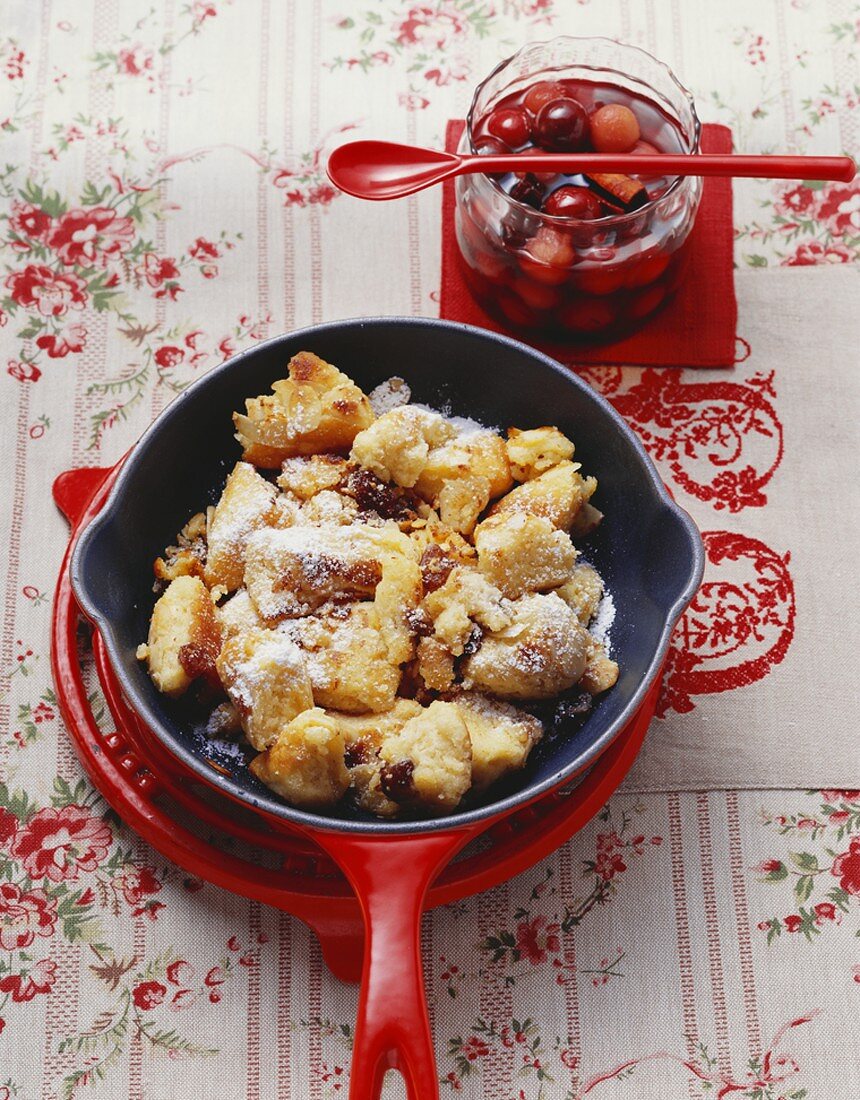 Semolina schmarren (pancake pieces) in frying pan, cherry compote in jar