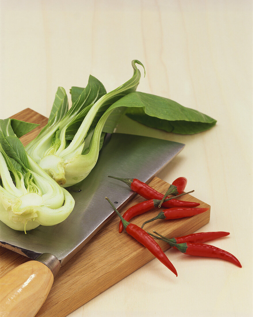 Pak Choi und Chilis auf Holzbrett mit asiatischem Messer