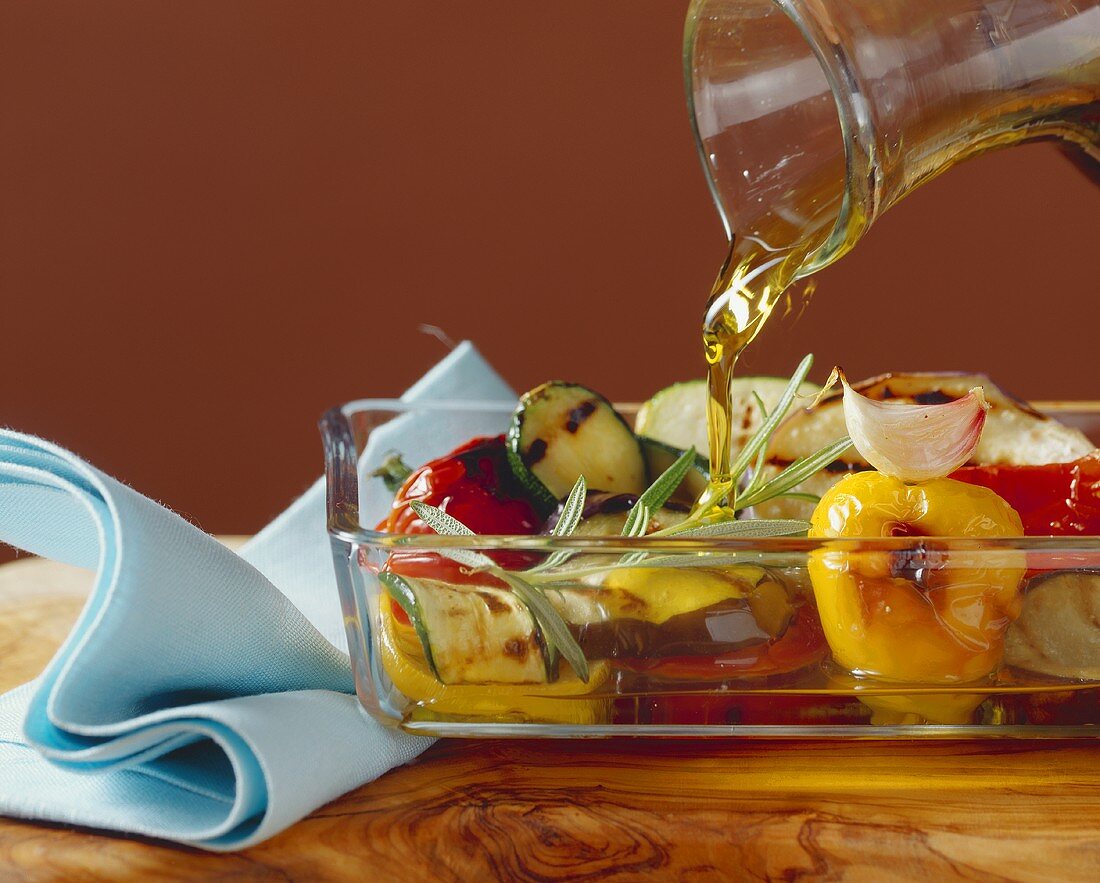 Pouring olive oil over antipasti vegetables in glass dish