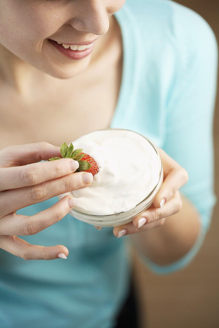 Young woman dipping a strawberry in yoghurt