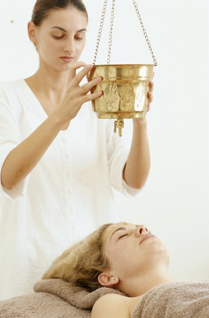 A masseuse pouring oil onto a woman's forehead
