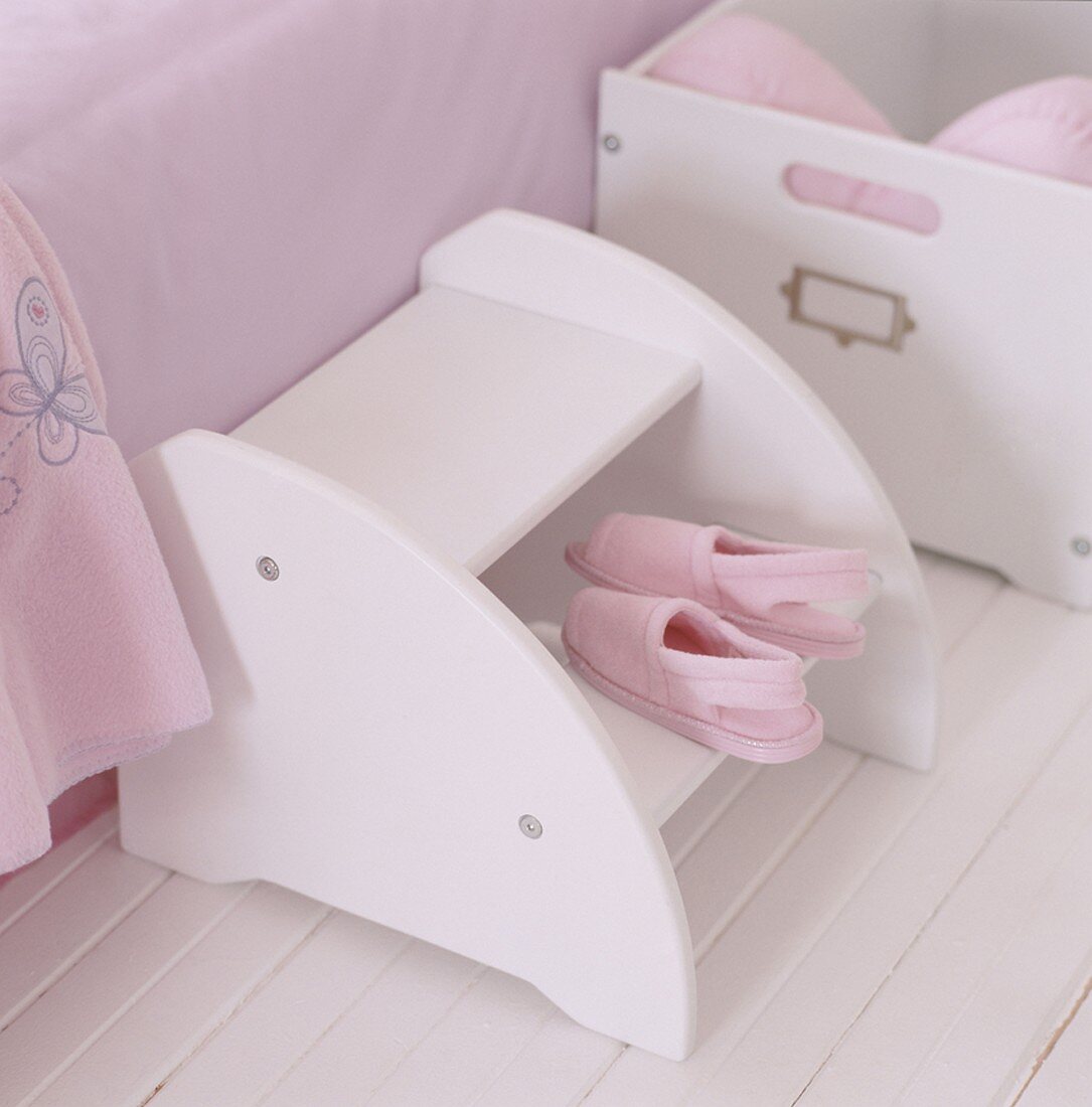 Pink slippers on a step stool by a bed