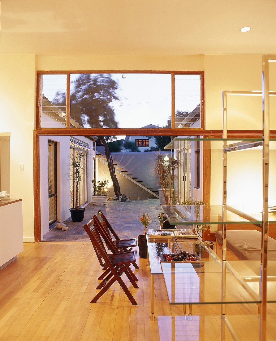 View from illuminated dining room with glass shelves and glass table into courtyard at twilight