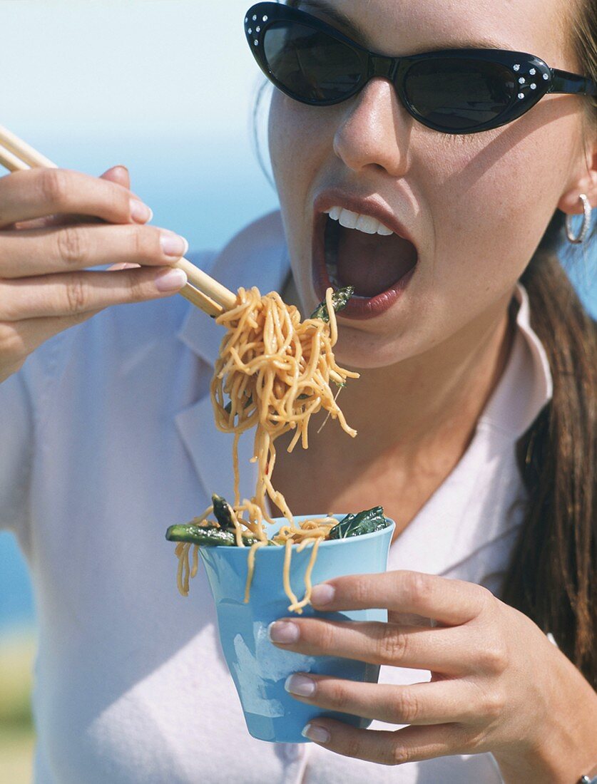 A young woman eating fried, oriental noodles with chopsticks