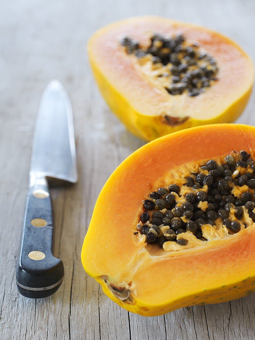 Two papaya halves and a knive on a wooden table
