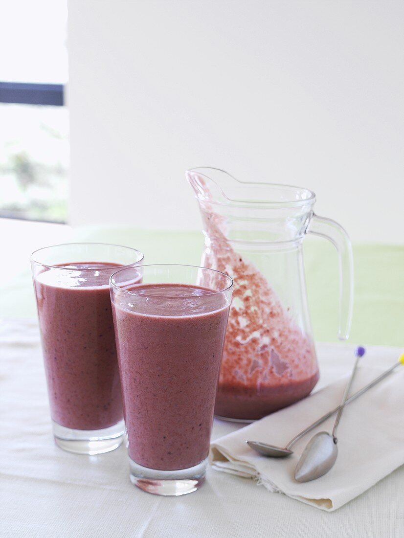 Berry smoothie in a glass jug and two glasses