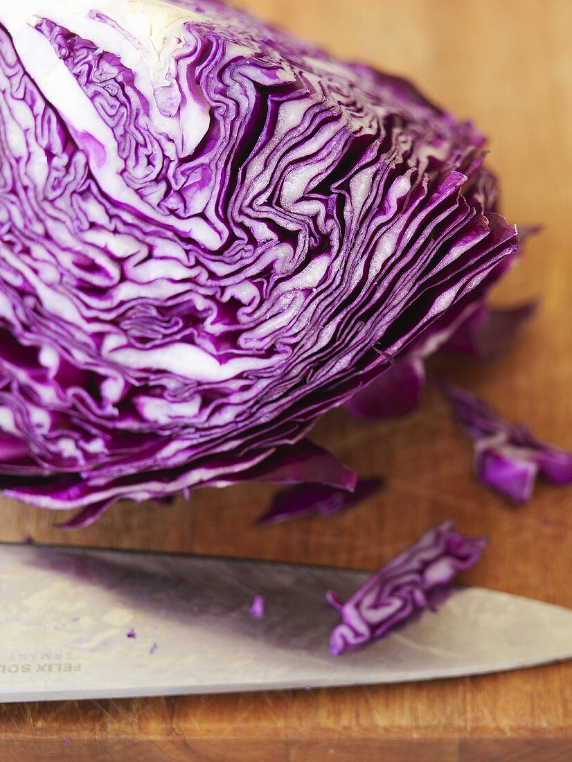 A section of red cabbage with knife on a chopping board