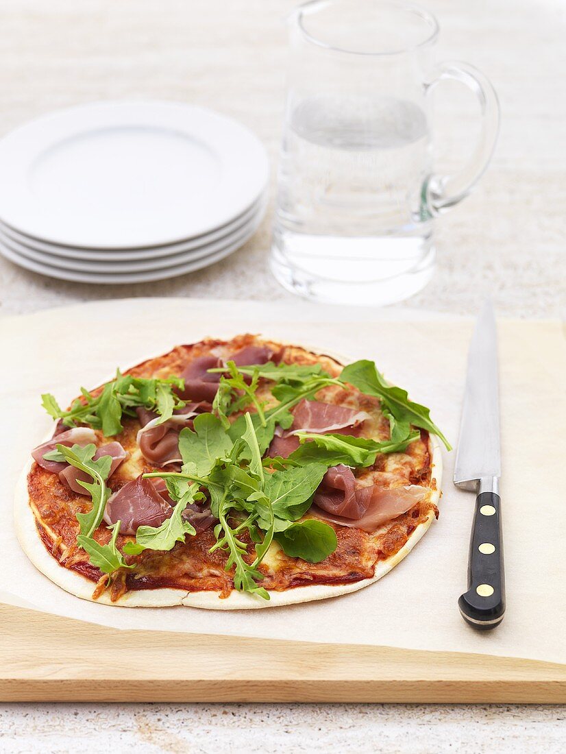 A pizza topped with ham and rocket on a chopping board