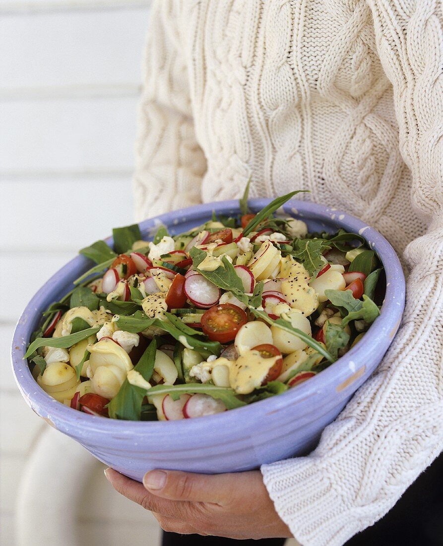 Person holding bowl of potato and rocket salad