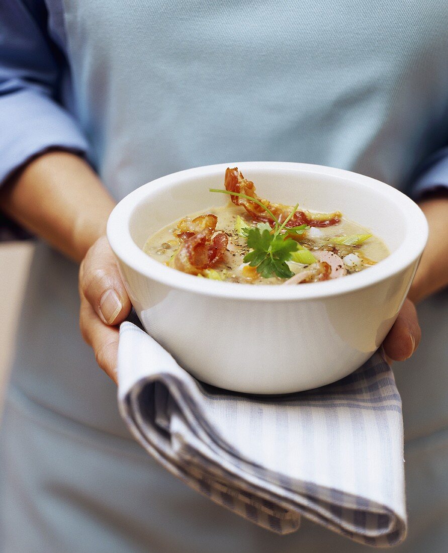 Hands holding a bowl of lentil stew with bacon