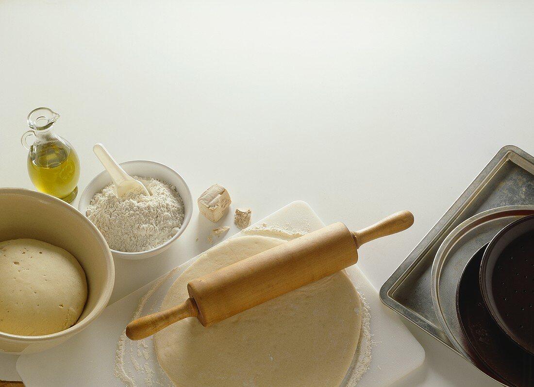 Rolled-out pizza dough with baking ingredients & baking trays