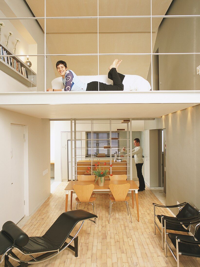 Man in open-plan kitchen, woman lying in front of sofa on mezzanine above