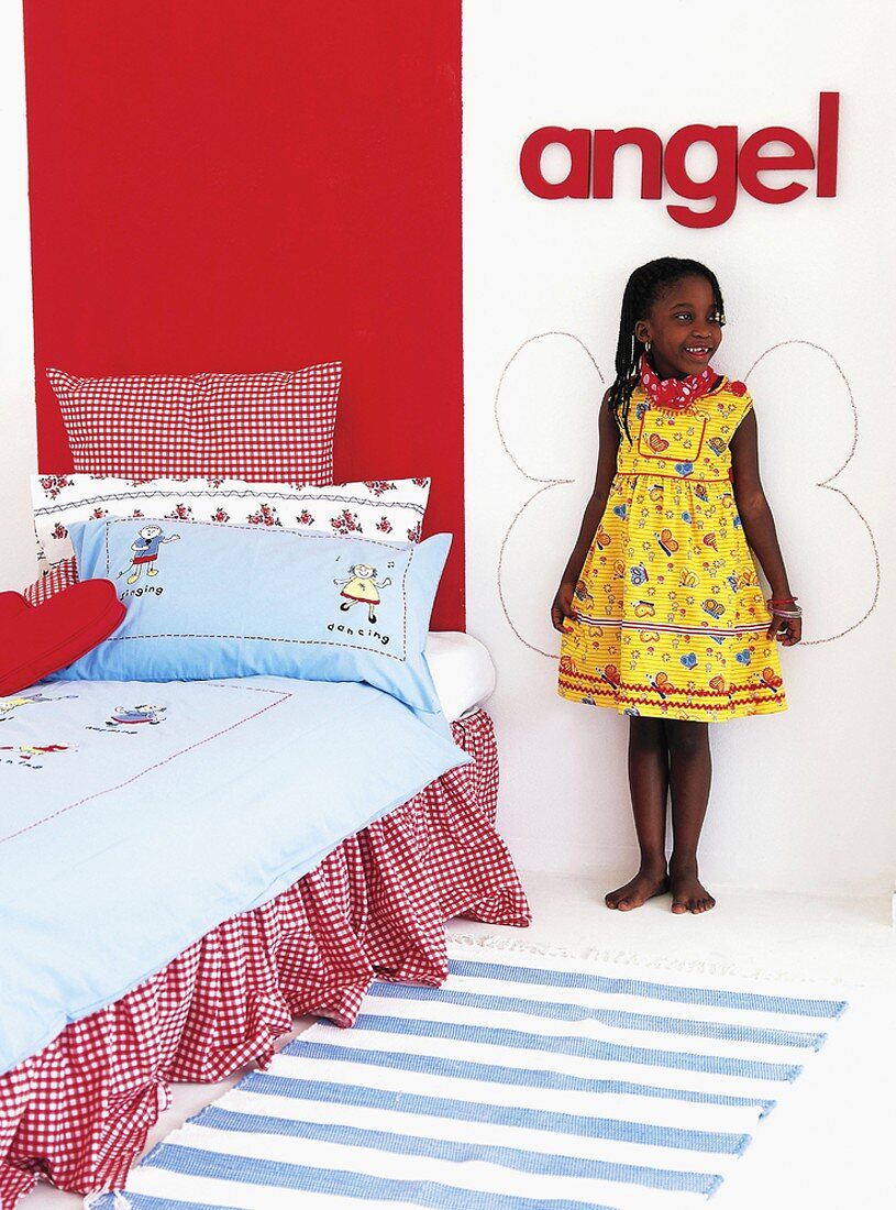 Girl standing in front of angels' wings painted on wall in child's bedroom