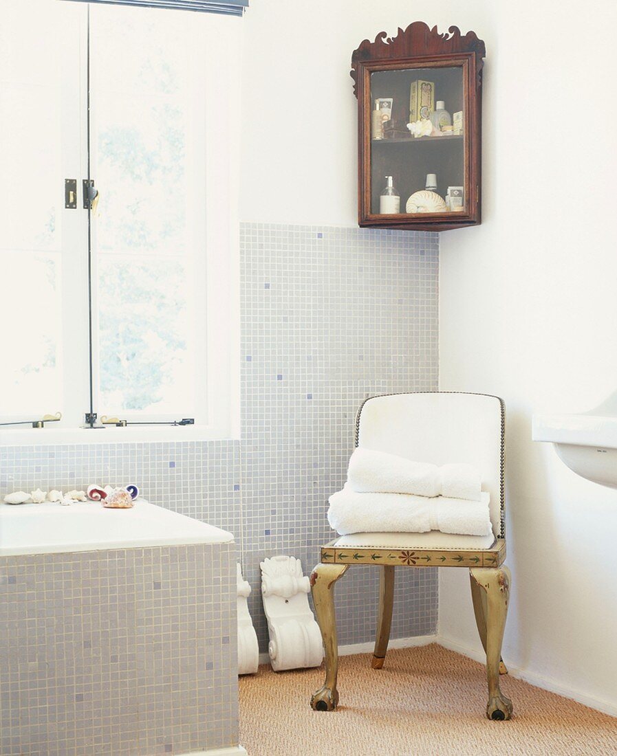 Mosaikgefliestes Badezimmer mit Eckvitrine, goldenem Stuhl und dekorativen Voluten