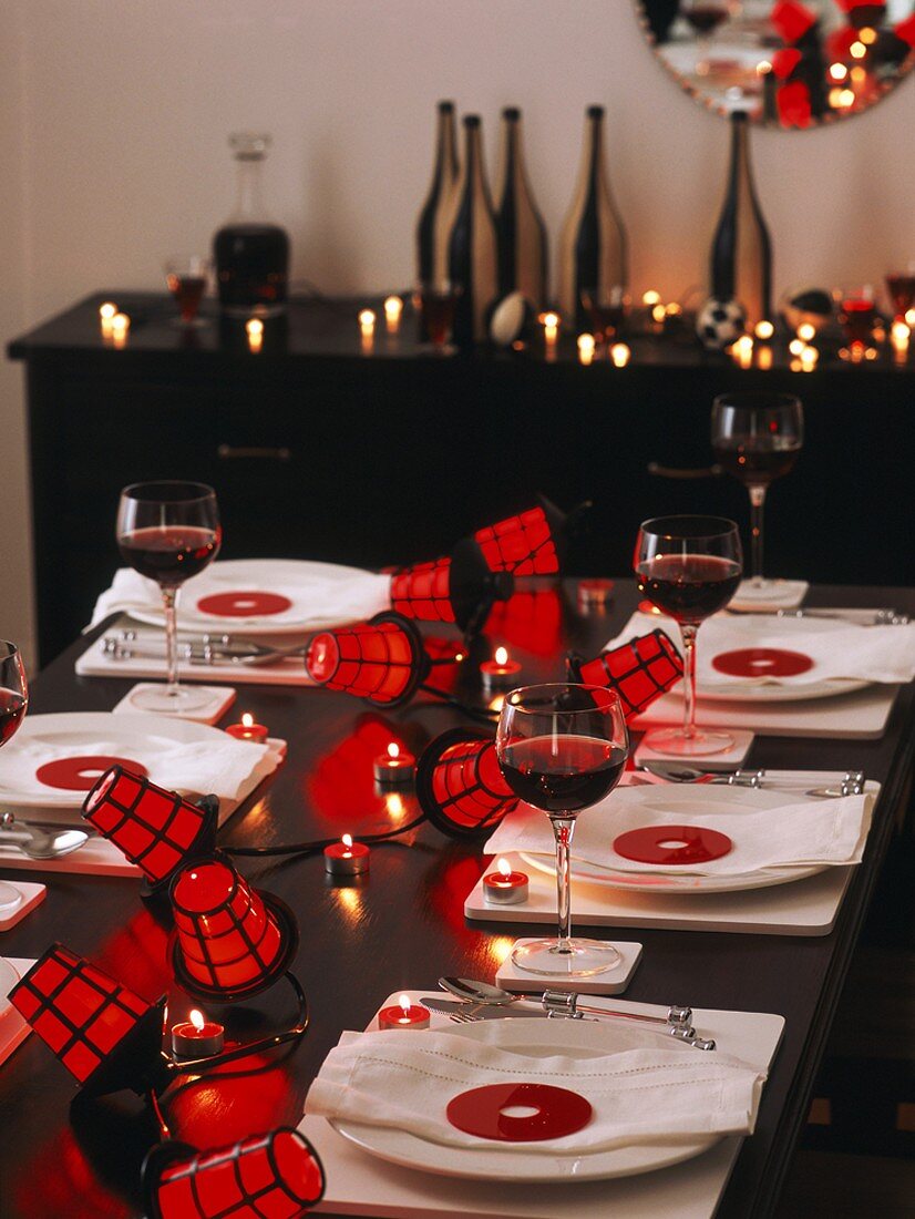 Einladend gedeckter Holztisch zu Halloween mit Rotweingläsern, Kerzenlicht und Lampions