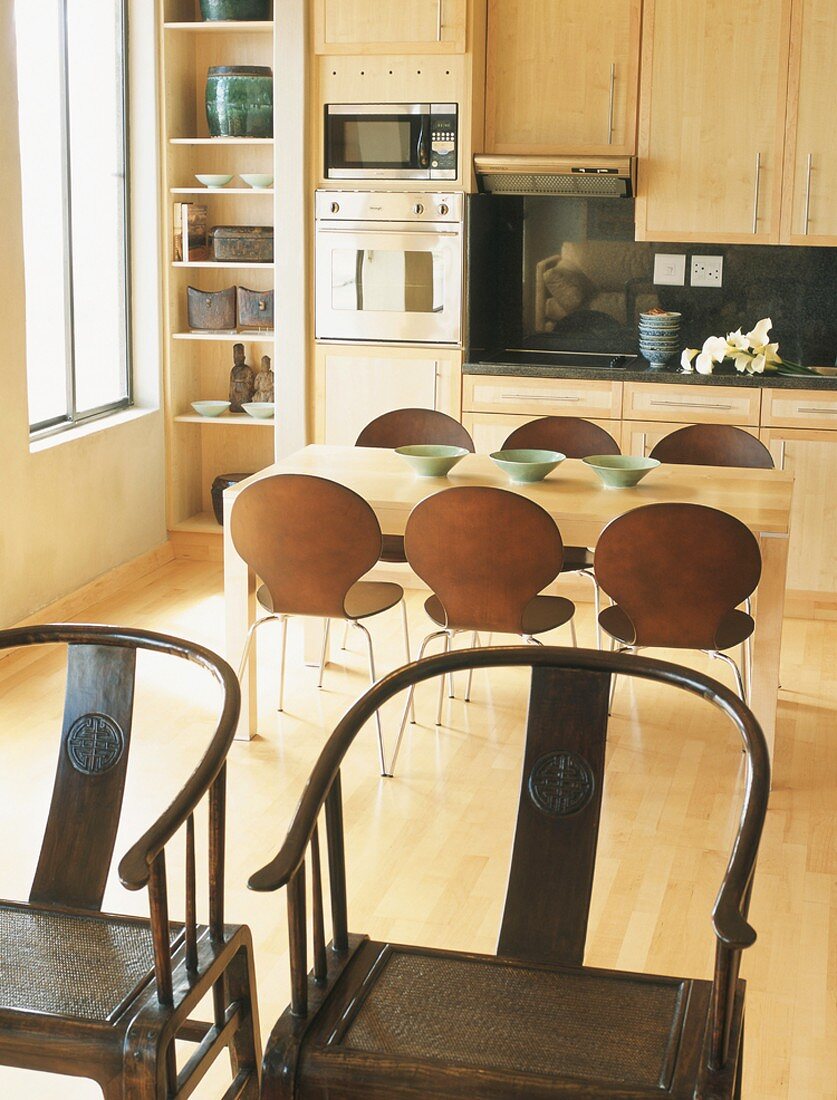 Moderne Einbauküche mit Holztisch und Designerstühlen hinter zwei antiken Holzstühlen