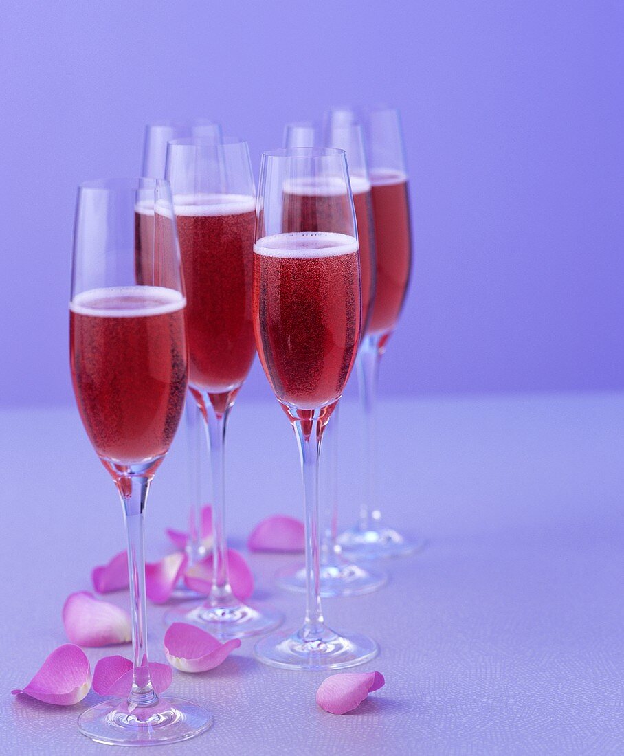 Mehrere Gläser rote Sekt-Cocktails mit Rosenblütenblätttern