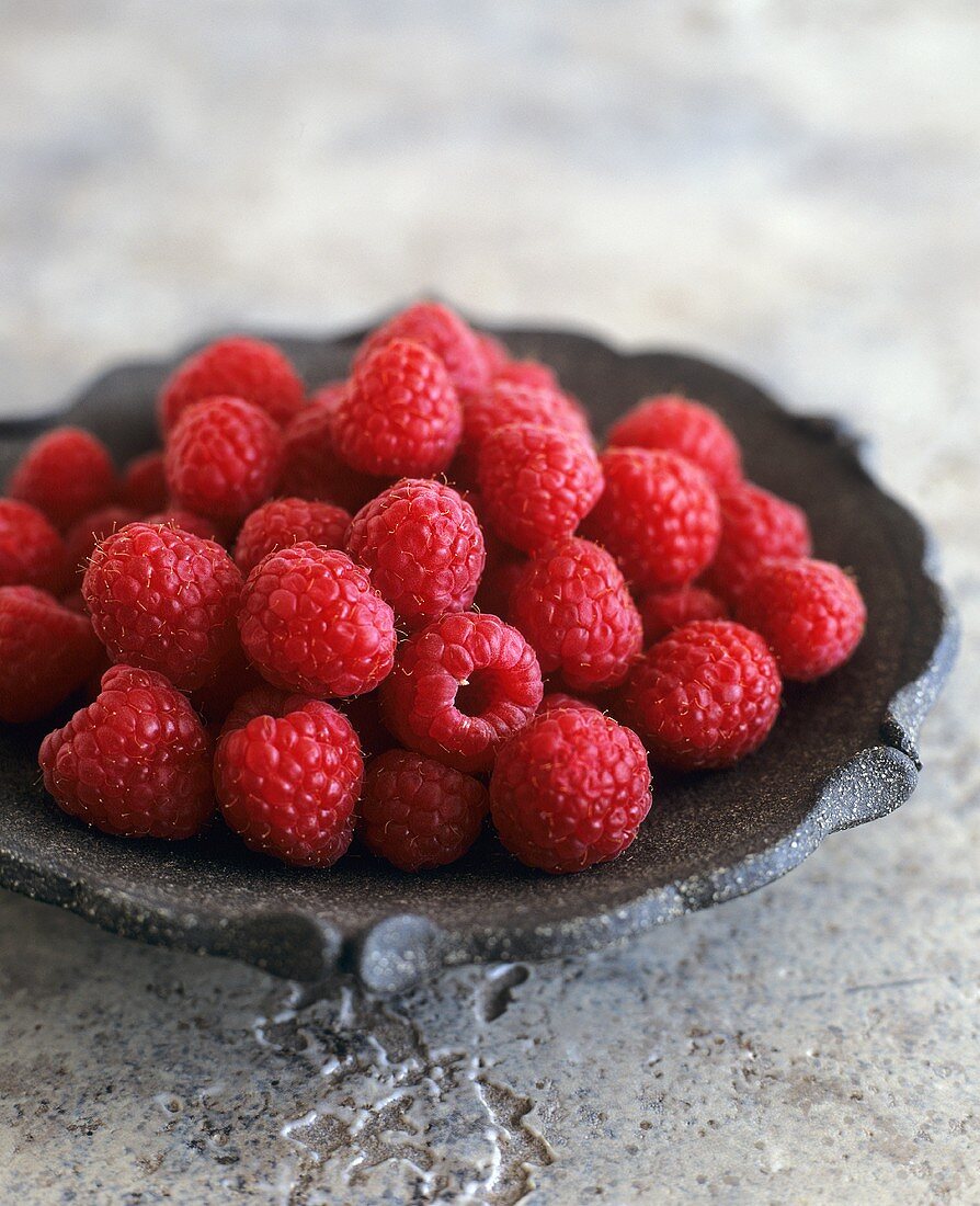 A plate of fresh raspberries on stone