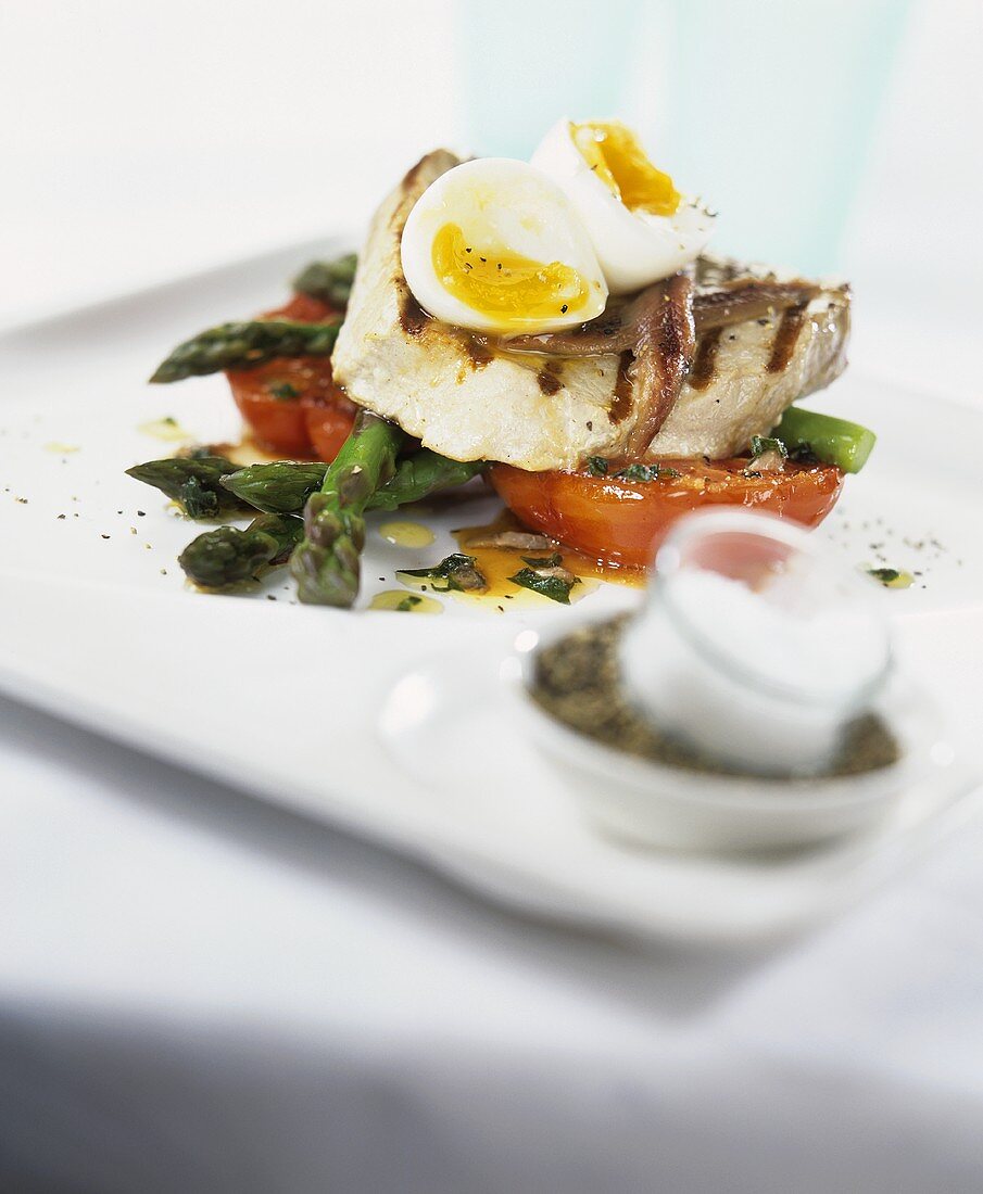 Grilled tuna steak with anchovies, egg, tomato and asparagus