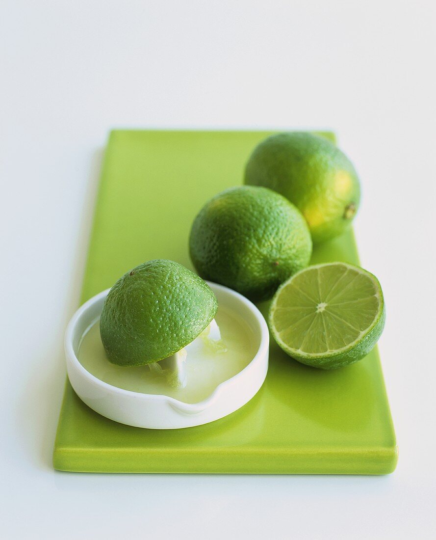 Limetten mit Zitruspresse auf grünem Küchenbrett