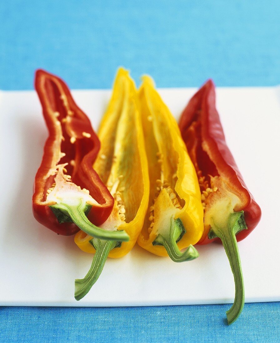 Halved red and yellow pointed peppers on chopping board