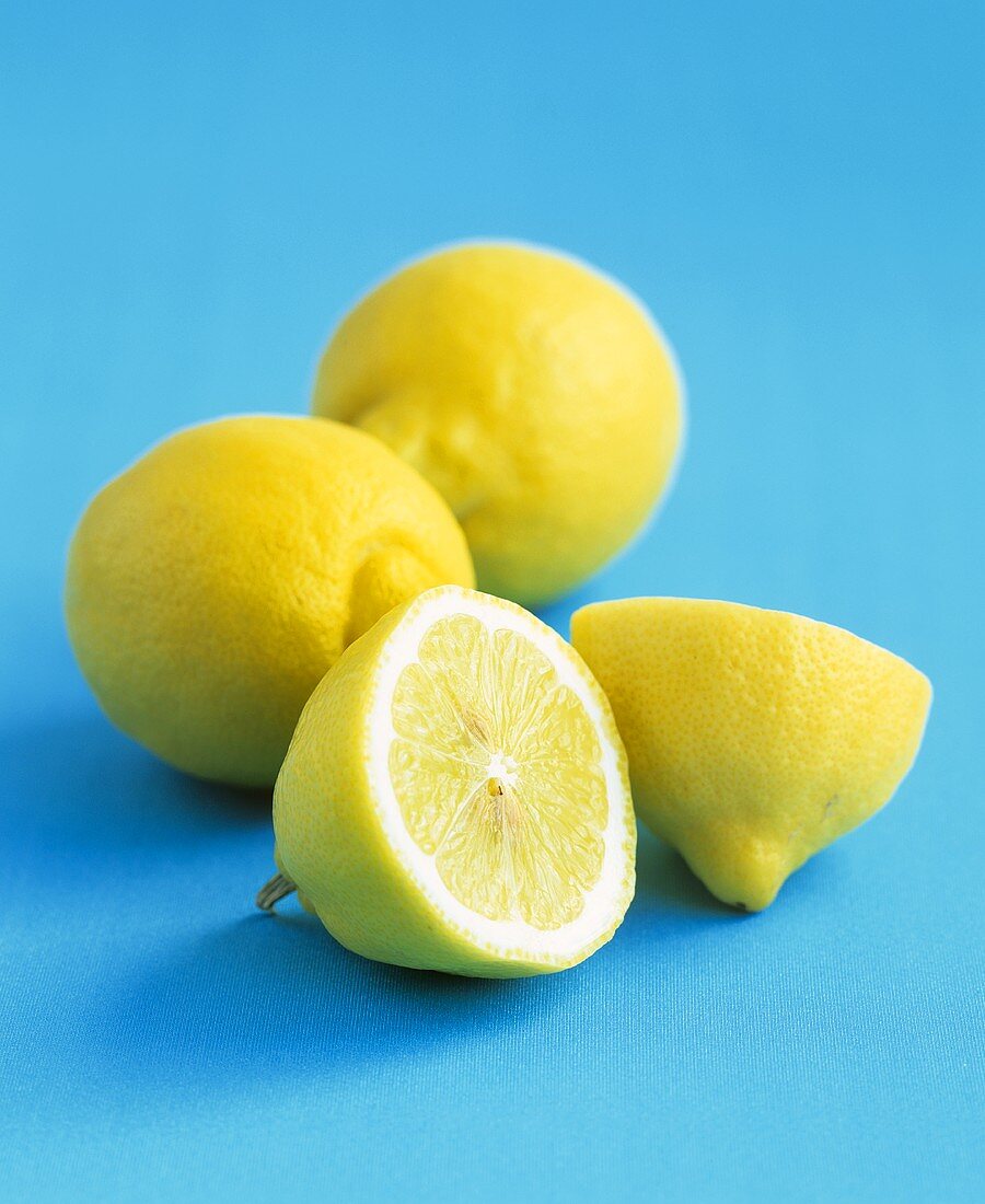 Zwei ganze und eine halbierte Zitrone vor blauem Hintergrund