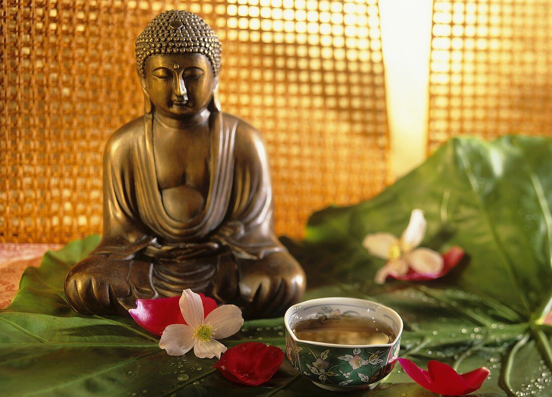 A bowl of pu-erh tea, flowers and Buddha figure