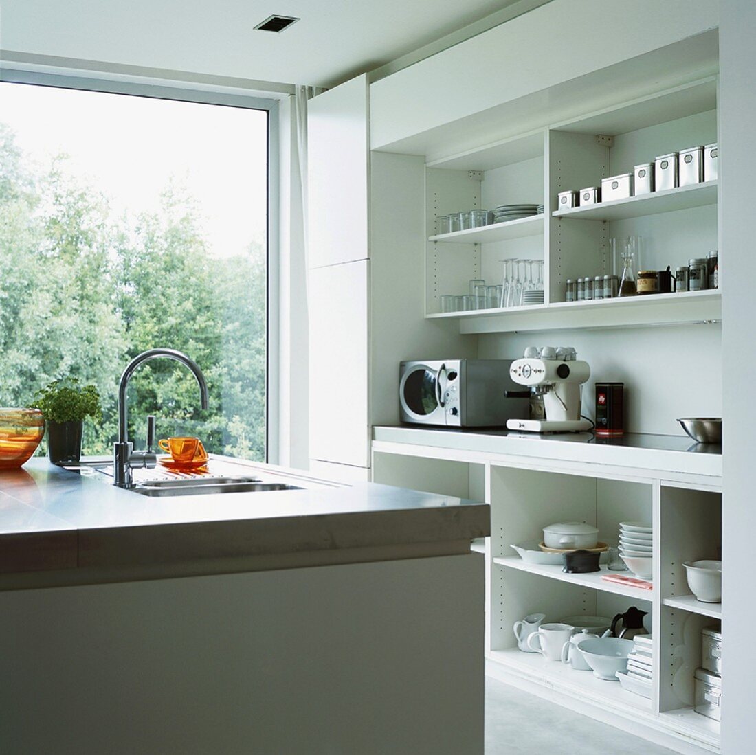 Durch das raumhohe Panoramafenster fällt viel Tageslicht in die moderne, weiße Küche