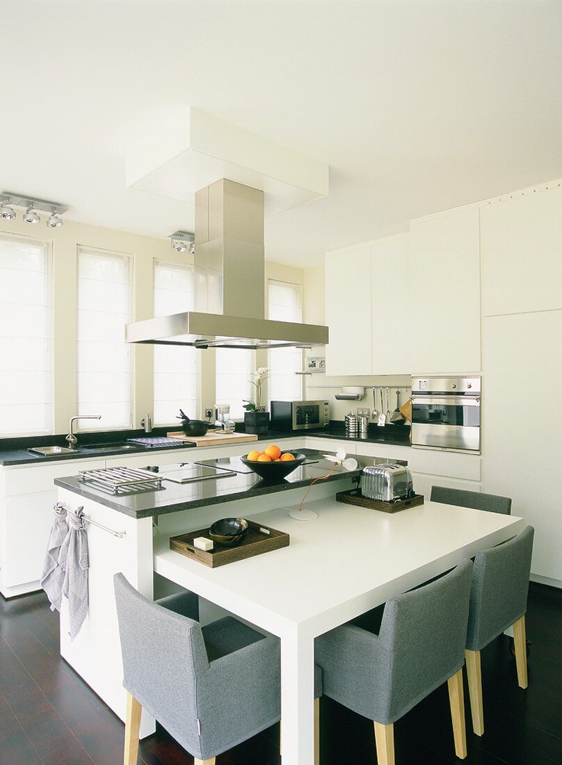 In der weissen Designerküche fügt sich ein minimalistischer Esstisch in den Küchenblock ein