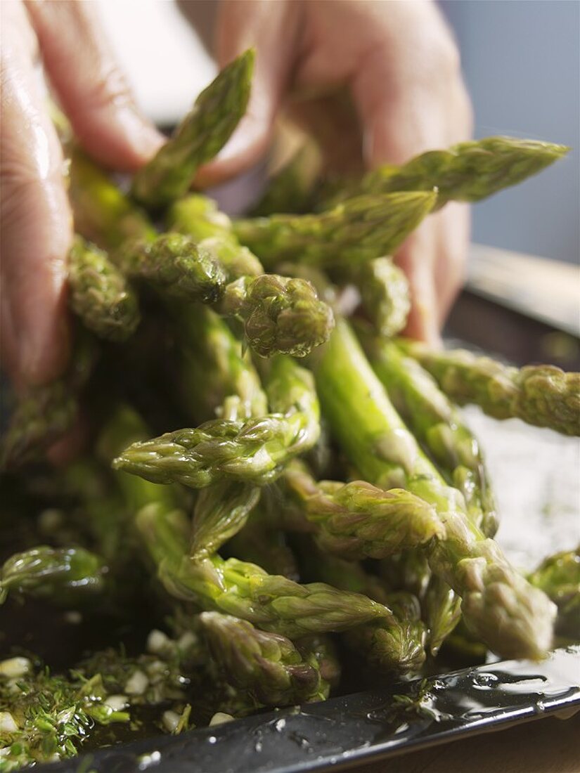 Hands putting cooked green asparagus on a plate