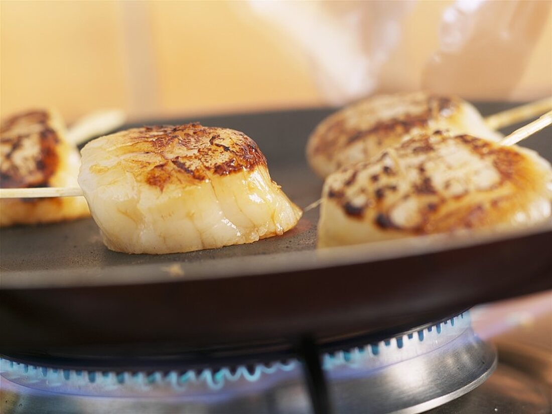 Frying scallops on small skewers in a frying pan