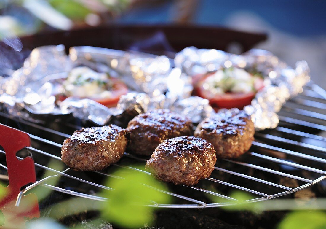 Hackbällchen und Tomaten in Folie auf dem Grill