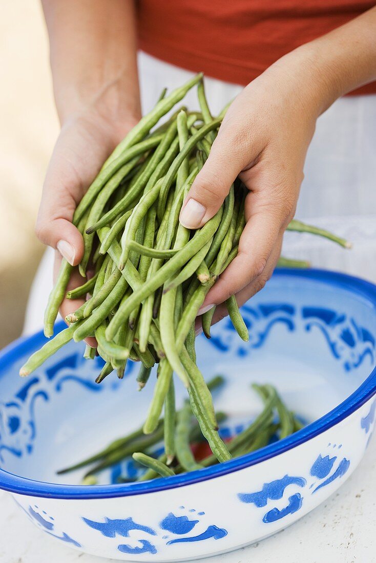 Hands putting green beans into a dish