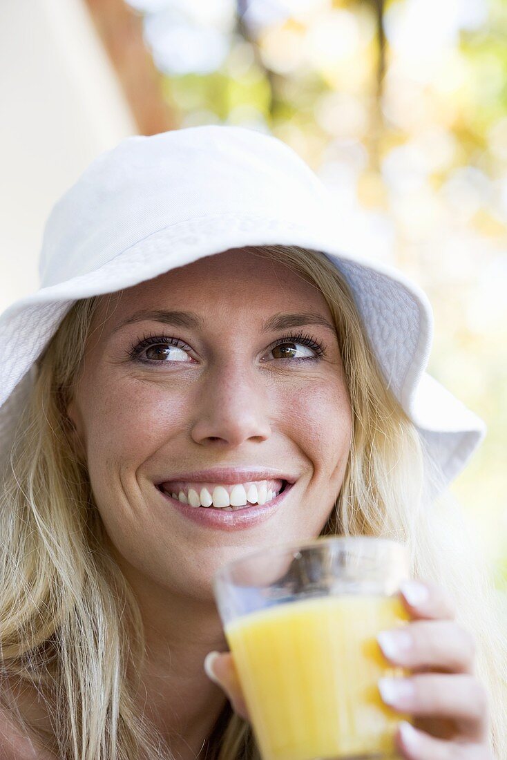 Frau mit Sommerhut trinkt ein Glas Orangensaft