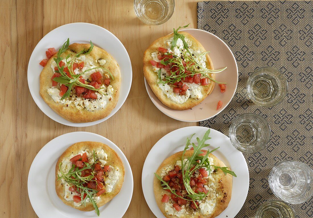 Four mini-pizzas topped with sheep's cheese, tomato & rocket