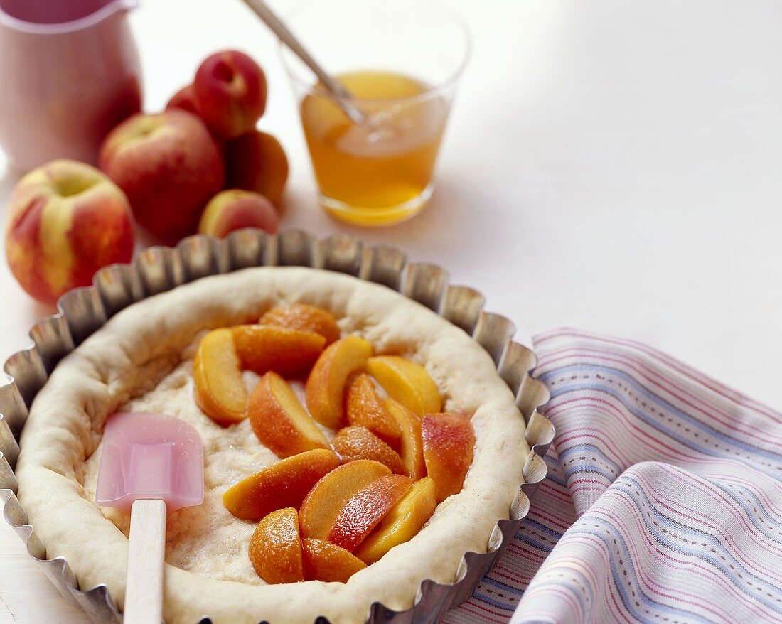 Uncooked dough topped with peach slices in a baking tin, 
