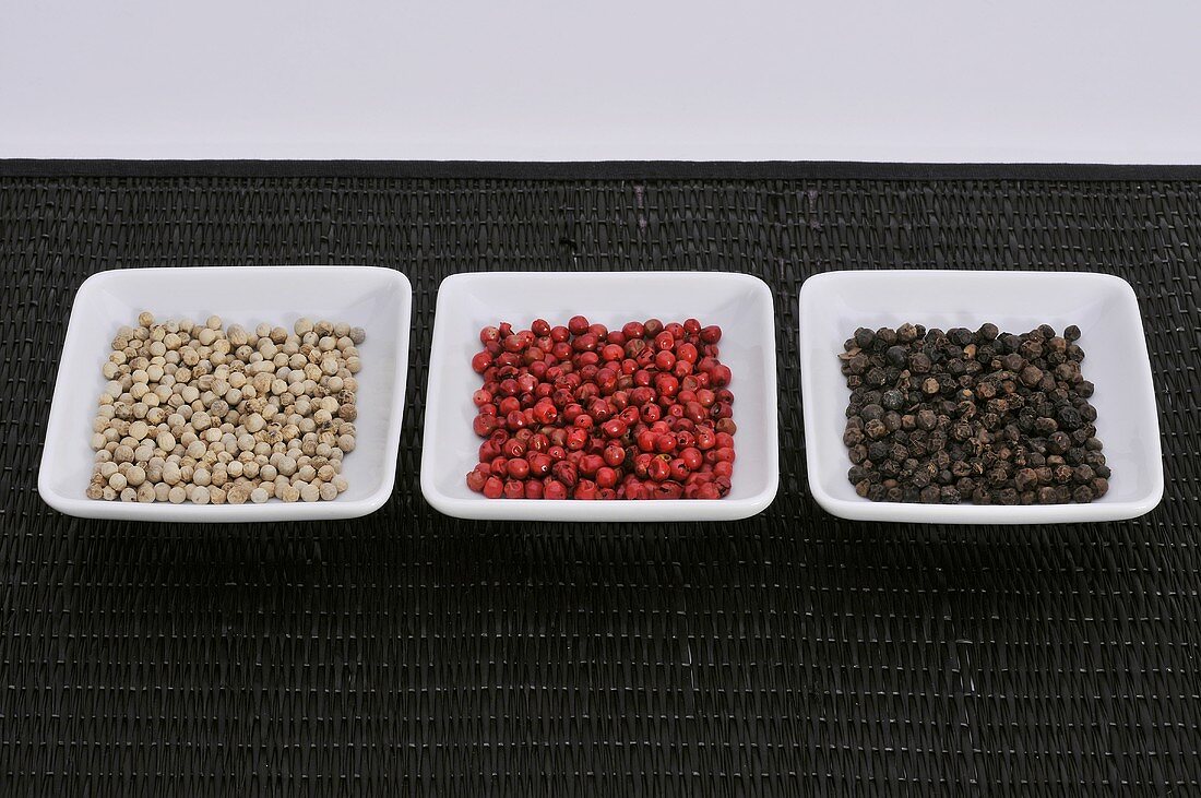 Black, red and white peppercorns in three dishes