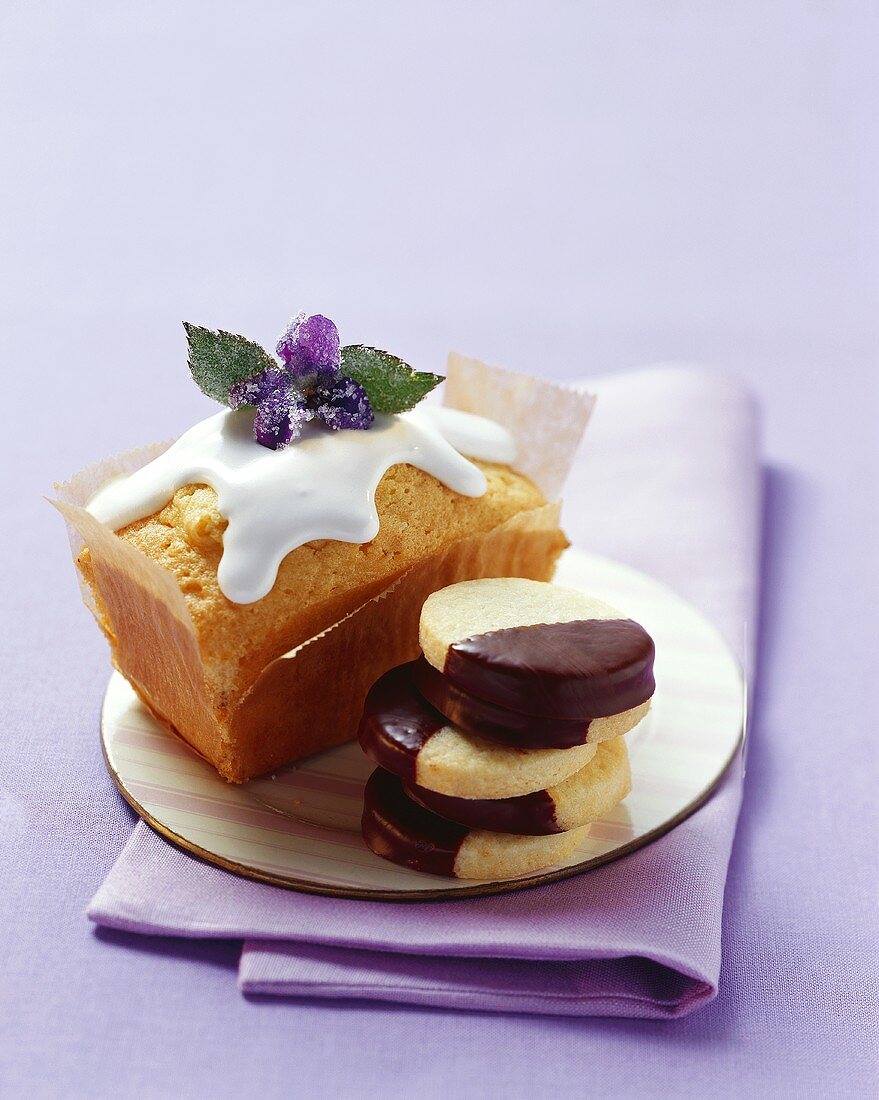 Iced cake with candied violet, chocolate-dipped biscuits
