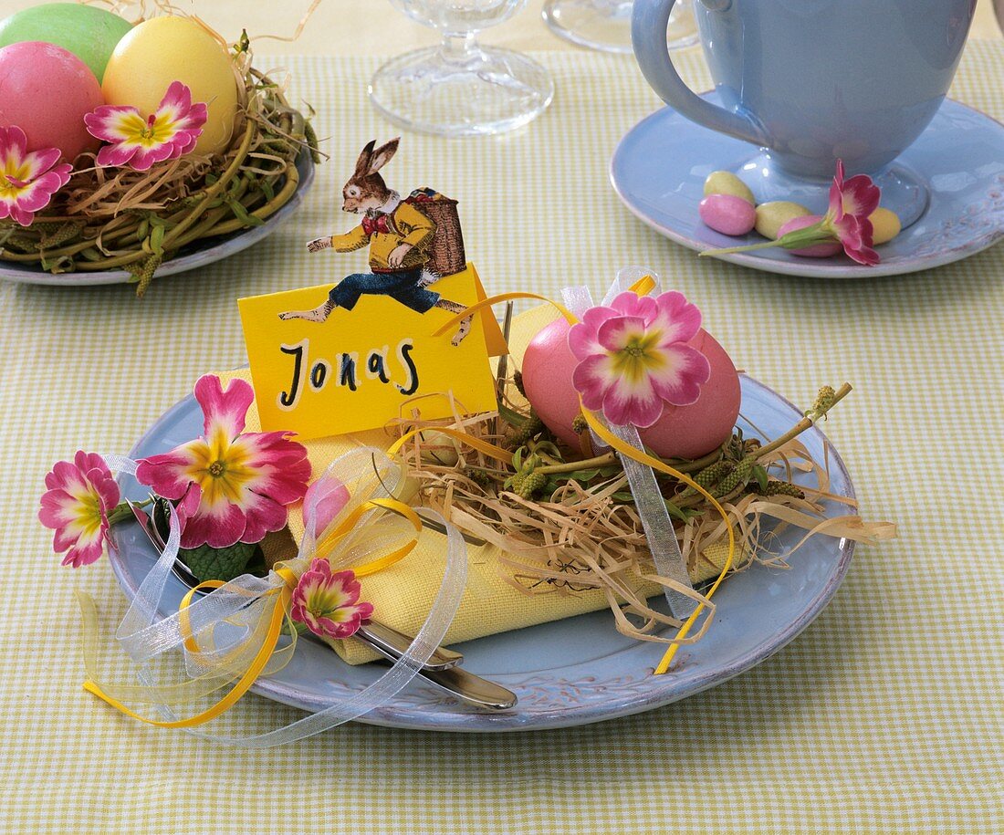Easter place-setting with primulas, hay, Easter egg & place card