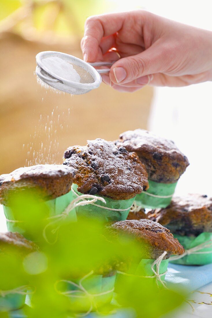 Hand siebt Puderzucker über Blaubeermuffins